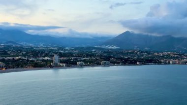 Huzurlu bir deniz manzarası görkemli dağlar, nazik dalgalar ve sakin bir gökyüzü.