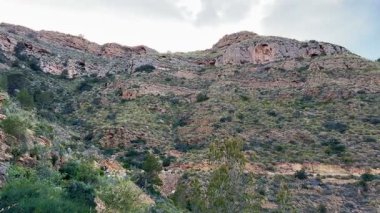 Huzurlu bir su kütlesine bakan nefes kesici dağ manzarası çarpıcı mavi gökyüzü ile çevrili.