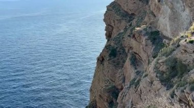 Çarpıcı manzara, kayalık uçurumların heybetli, berrak mavi gökyüzünün altında sakin denizle çarpıştığını gösteriyor.