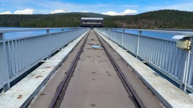 Huzurlu bir köprü manzarası, sakin bir su, canlı doğa ve parlak mavi gökyüzü ile çevrili.