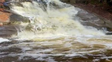 Engebeli kayaların üzerinde çağlayan muhteşem bir şelale manzarası. Altından köpüklü su akıyor.