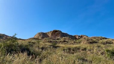 Altın otlarla bezenmiş kayalık tepelerin nefes kesici manzarası açık mavi gökyüzünün altında güzel bir şekilde uzanıyor.