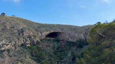 Yeşillik ve görkemli kayalık tepelerle çevrili büyüleyici ve nefes kesici bir mağara manzarası.