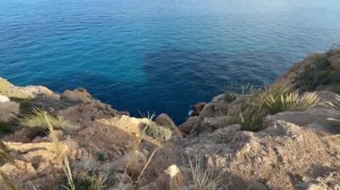 Sakin mavi sulara ve yukarıdaki berrak gökyüzüne tepeden bakan dramatik kayalıkların nefes kesici manzarası.