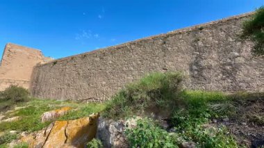 Açık mavi gökyüzünün altında canlı yeşilliklerle çevrili etkileyici antik taş bir duvar nefes kesici bir manzara sunuyor.