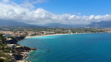 Kristal berrak turkuaz suları ve dingin plajlarıyla el değmemiş bir kıyı şeridini gösteren nefes kesici bir hava manzarasının tadını çıkarın.