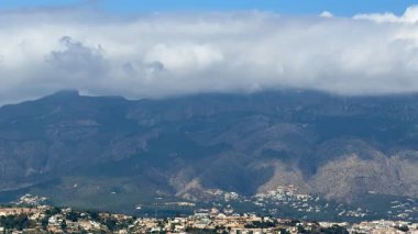 Güzel bir dağ manzarası pofuduk bulutları ve berrak gökyüzünü huzur dolu bir vadide barındırır.