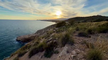 Huzurlu suları ve engebeli kıyı şeridini aydınlatan muhteşem bir gün batımının nefes kesici manzarasına tanık olun.
