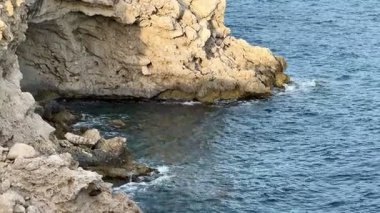 Büyüleyici ve nefes kesici manzara dalgaların yavaşça kıyıya vurduğu engebeli bir kayalık kıyı şeridini gösteriyor.