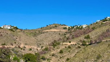 Parlak mavi gökyüzü ve güneş ışığına karşı güzel bir şekilde dizilmiş lüks evleri gösteren yuvarlanan tepelerin çarpıcı manzarası.