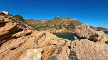 Nefes kesici bir kayalık kıyı şeridi berrak mavi sularla birlikte parlak bir gökyüzünün altında canlı bir manzara sergiliyor.