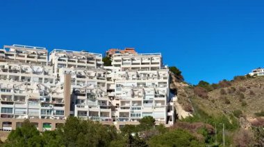 Berrak mavi gökyüzünün altında modern evlerle dolu nefes kesici manzaralı bir tepe manzarası.