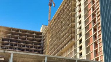 Turnalarla dolu canlı bir inşaat alanı ve yukarıdaki açık mavi gökyüzünün altında kısmen inşa edilmiş bir yapı.