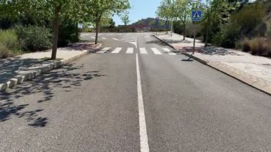 Berrak ve belirgin yaya geçişlerinin ve yemyeşil ağaçların yer aldığı güneşli bir yol manzarası.