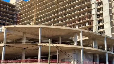 Etkin bir inşaat alanının dinamik bir görüntüsü büyük vinçleri ve geniş yapı iskeletlerini gösteriyor