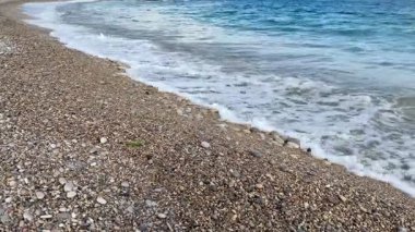Güzel, sakin bir sahil sahnesinde yumuşak çakıl taşları ve yumuşak dalgalar kıyıya hafifçe vuruyor.