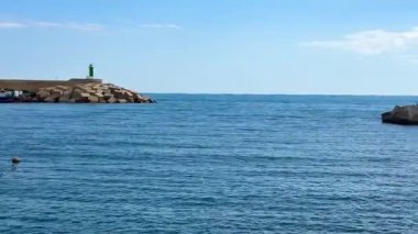 Berrak mavi okyanus sularının kıyısındaki kayalık bir iskelede görkemli bir deniz feneri barındıran sakin bir kıyı manzarası.
