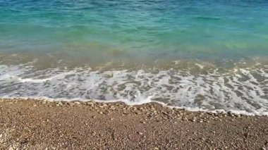 Yumuşak dalgaların huzur veren manzarasının tadını çıkarın. Açık mavi gökyüzünün altında çakıl taşlı kıyılara çarpan dalgaların.
