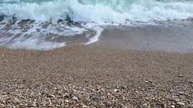 Yumuşak dalgalar hoş, çakıllı bir plaja hafifçe çarpıyor, güzel ve sakin bir sahil atmosferi yaratıyor.