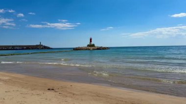 Güzel kıyı manzarası sergiliyor çarpıcı bir deniz feneri, sakin sular ve tepemizde parlak mavi bir gökyüzü.