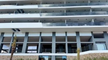 Modern, çok katlı bir binada parlak ve parlak mavi gökyüzüne karşı yapılmış kıvrımlı balkonlar sergileniyor.