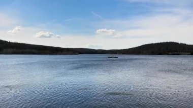 Berrak mavi bir gökyüzünün altında yemyeşil tepelerle çevrili sakin bir gölün nefes kesici güzelliği.