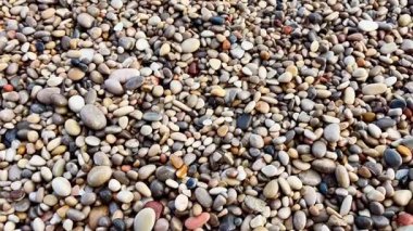 Çakıl taşlı bir kıyı şeridinin pitoresk manzarası kumlu sahilde hafif dalgaların hafifçe dalgalandığını gösteriyor.