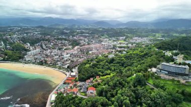 Büyüleyici bir hava görüntüsü, büyüleyici bir sahil kasabasını, çarpıcı bir sahil ve yemyeşil tepeleri aydınlatıyor.