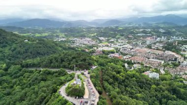Hava görüntüleri, yeşil tepeler ve deniz kıyısındaki dağların arasına kurulmuş canlı bir kıyı şehrini gösteriyor.