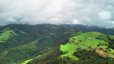 Nefes kesen hava görüntülerinde canlı yeşil manzaralar ve bulutlu gökyüzünün altında yuvarlanan tepeler görülüyor.