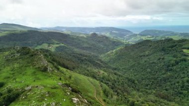 Nefes kesen manzara bulutlu bir gökyüzünün altındaki dingin denize inen yemyeşil dağları gösteriyor.