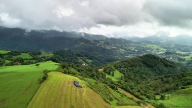 Bulutlu gökyüzünün altındaki yeşil tepeleri ve vadileri gösteren nefes kesici hava manzarasını deneyin.