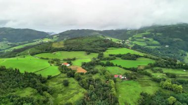 Sersemletici hava görüntüleri güzel bir şekilde sergileniyor canlı yeşil tarlalar ve yuvarlanan tepeler bulutlu bir gökyüzüne karşı.