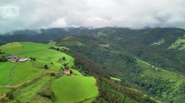 Nefes kesen hava manzarası yuvarlanan yeşil tepeler ve bulutlu bir gökyüzünün altında manzaralı tarım arazileri..