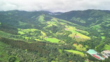 Bulutlu gökyüzünün altındaki yemyeşil tepelerin ve vadilerin büyüleyici hava görüntüleri güzellikleri sergiliyor..