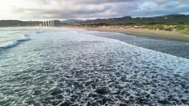 Dinginlik için ideal altın saat boyunca dalgalar ve canlı bulutlarla sakin bir sahil sahnesi.