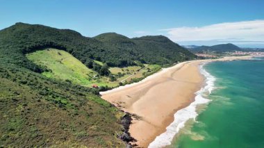 Bereketli tepeler ve berrak sularla çevrili güzel ve sakin bir plajın çarpıcı hava manzarası.