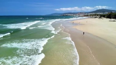 Sakin bir plajı ve berrak gökyüzünün altında canlı turkuaz suları gösteren nefes kesici bir hava görüntüsü..