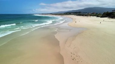 Yumuşak dalgaların oluşturduğu nefes kesici bir sahil manzarası altın kumda yavaşça kırılıyor ve sakin bir atmosfer yaratıyor.