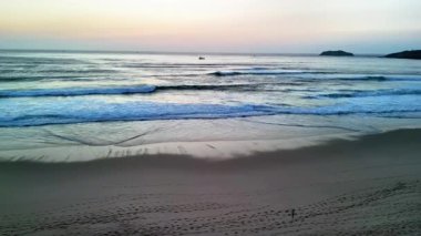 Gün batımında sakin bir sahil sahnesinde hafif dalgalar sahneyi okşuyor ve güzel renklerle parlayan bir gökyüzü.