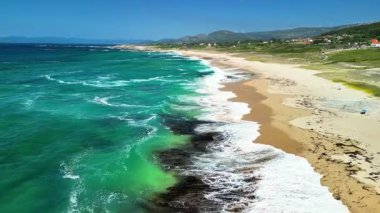 Hava manzarası, turkuaz dalgalarla çerçevelenmiş ve yemyeşil manzaralarla çevrili çarpıcı bir kumsal sergiliyor.