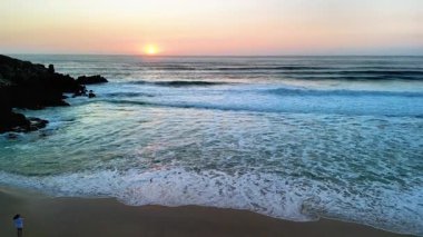 Gün batımının çarpıcı görüntüsü sakin ve sakin bir kumsalın sakin dalgalarını güzel bir şekilde yansıtıyor.