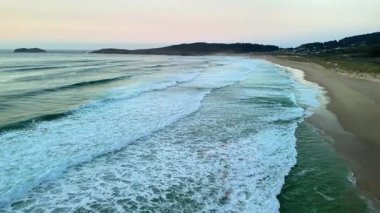 Nefes kesici ve çarpıcı bir hava görüntüsü güzel bir şekilde sergileniyor. Pastel günbatımı gökyüzünün altında sakin okyanus dalgaları.