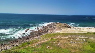 Kayalık bir kıyı şeridinin ve güzel okyanusun güneşli gününde dalgaların tadını çıkar.