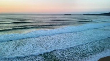Güneş güzel bir şekilde batarken sakin ve sakin bir plajda usulca süzülen yumuşak okyanus dalgalarının çarpıcı görüntüsü.