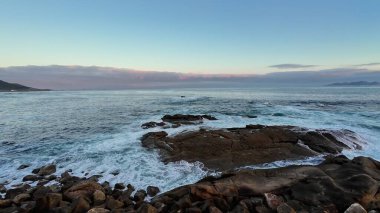 Huzurlu ve huzurlu bir sahil manzarası. Huzurlu bir günbatımı gökyüzünün altında kayalık kıyılara vuran yumuşak dalgaların olduğu.