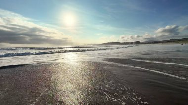 Şaşırtıcı derecede sakin bir sahil manzarası parlak güneşin altında parıldayan dalgalar sergiliyor, saf huzur ve sükuneti çağrıştırıyor.