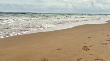 Yumuşak, sıcak kumlarla, yumuşacık dalgalarla ve güzel, sakin, bulutlu gökyüzüyle karakterize edilmiş sakin bir sahil.