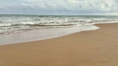 Yumuşak, sıcak kumlu, yumuşak dalgalı, karamsar gökyüzünün yanında dalgalı büyüleyici bir sahil manzarası.