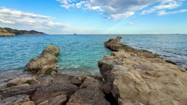Berrak suları ve gökyüzünün huzur dolu sükunetiyle kayalık bir sahil şeridinin nefes kesici güzelliğini hissedin.